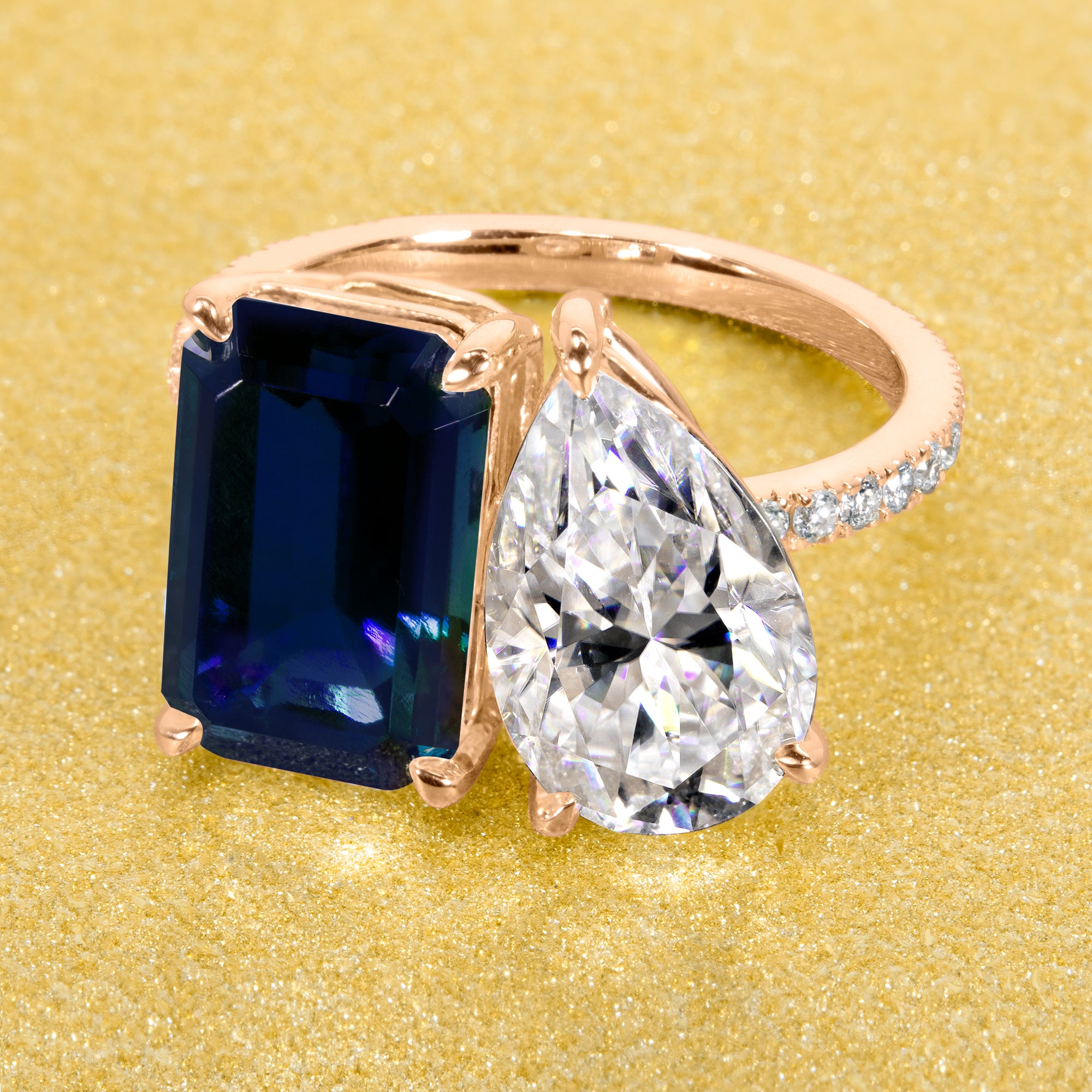 This timeless "Toi et Moi" Gemini engagement ring showcases a captivating combination of a 3.75ct lab-grown elongated emerald-cut blue sapphire and a 2.25ct pear-shaped moissanite, styled with lab-grown side diamonds. The ring is available in 14K Gold, 18K Gold, or Platinum by Earthena Jewelry of Beverly Hills.