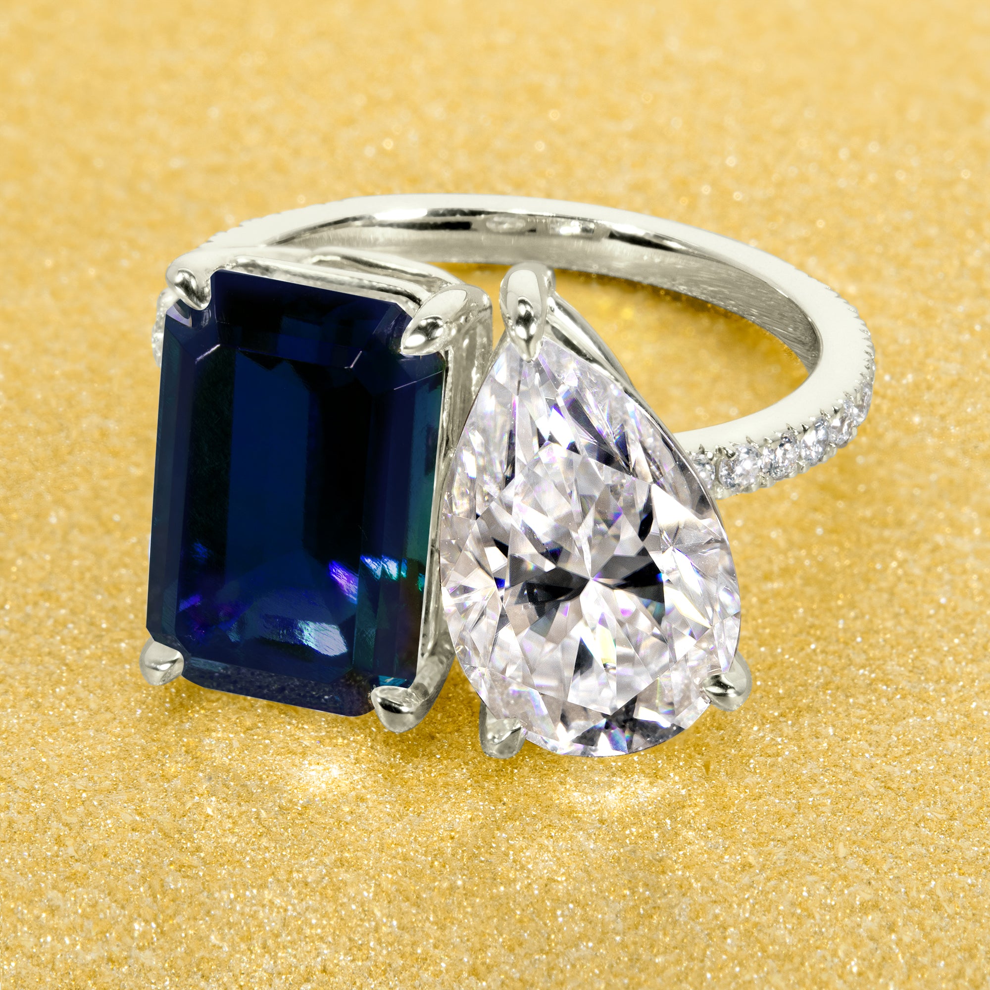 This timeless "Toi et Moi" Gemini engagement ring showcases a captivating combination of a 3.75ct lab-grown elongated emerald-cut blue sapphire and a 2.25ct pear-shaped moissanite, styled with lab-grown side diamonds. The ring is available in 14K Gold, 18K Gold, or Platinum by Earthena Jewelry of Beverly Hills.