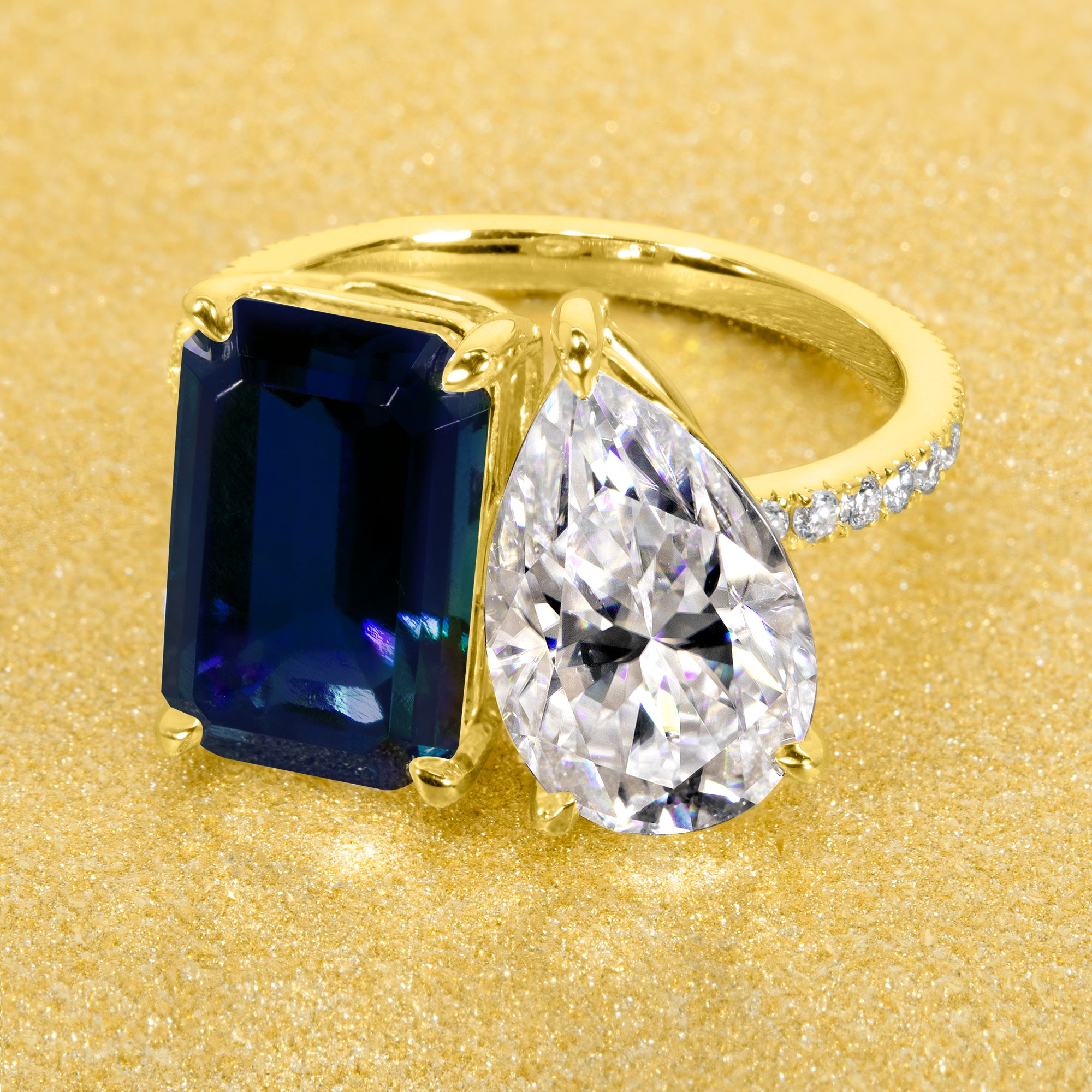 This timeless "Toi et Moi" Gemini engagement ring showcases a captivating combination of a 3.75ct lab-grown elongated emerald-cut blue sapphire and a 2.25ct pear-shaped moissanite, styled with lab-grown side diamonds. The ring is available in 14K Gold, 18K Gold, or Platinum by Earthena Jewelry of Beverly Hills.