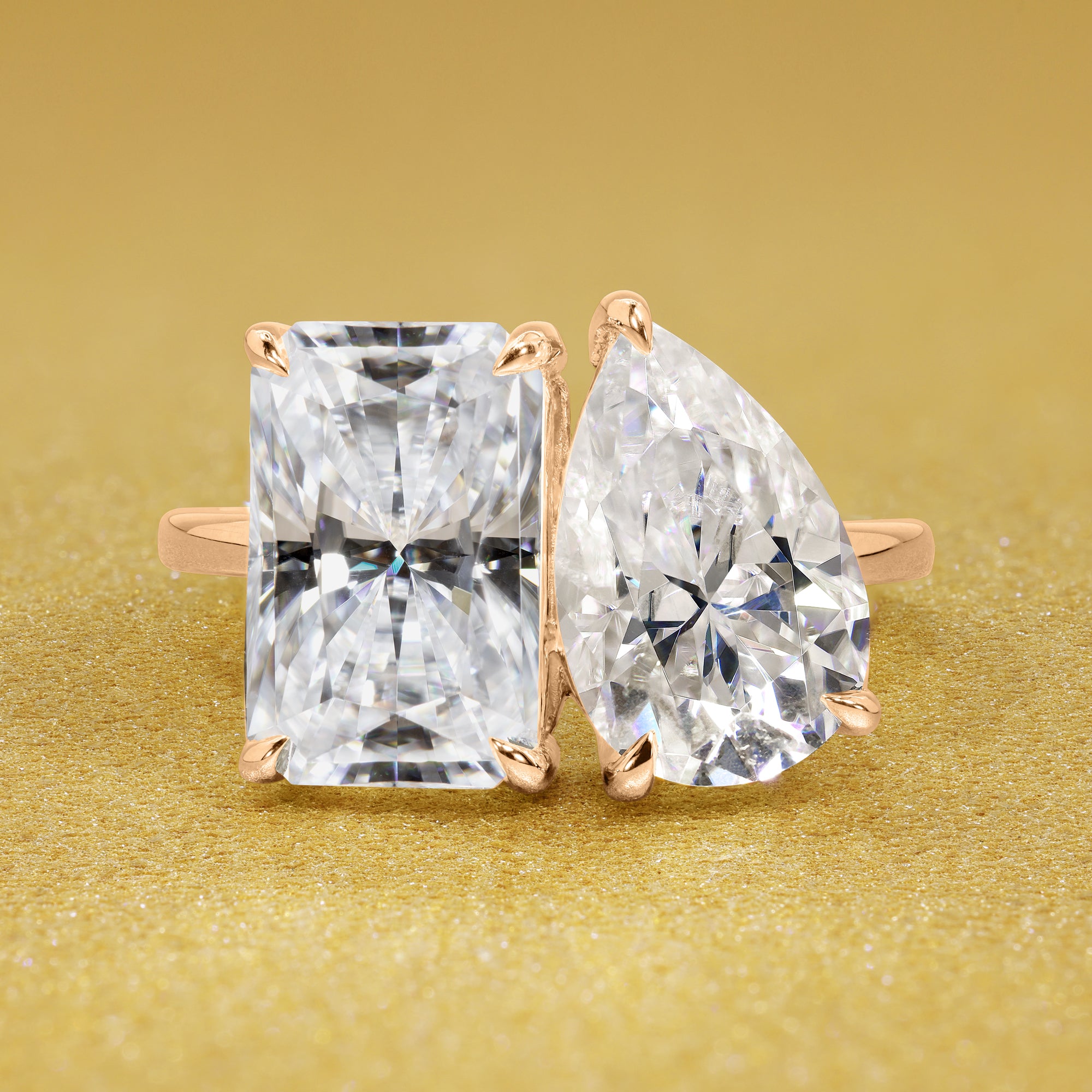 This timeless "Toi et Moi" Gemini engagement ring showcases a captivating combination of a 3.75ct elongated radiant-cut and a 2.25ct pear-shaped moissanite in a minimalistic plain gold band setting. The ring is available in 14K Gold, 18K Gold, or Platinum by Earthena Jewelry of Beverly Hills.
